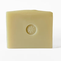 A bar of Coriander soap, embossed with TONIC's sun flower logo, on a white background.