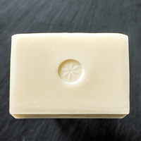 Naked unscented bar soap unwrapped on a black slate background