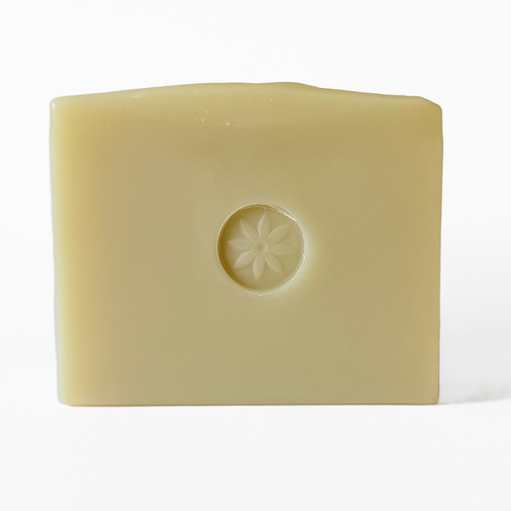A bar of Coriander soap, embossed with TONIC's sun flower logo, on  a white background.