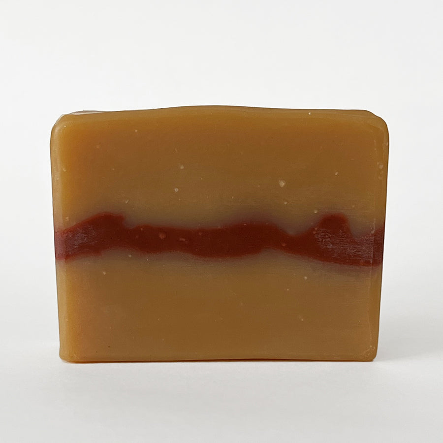 The unstamped side of an unwrapped bar of Rockrose Bar Soap, displaying the brick red wavy layer running through the deep golden amber soap. 